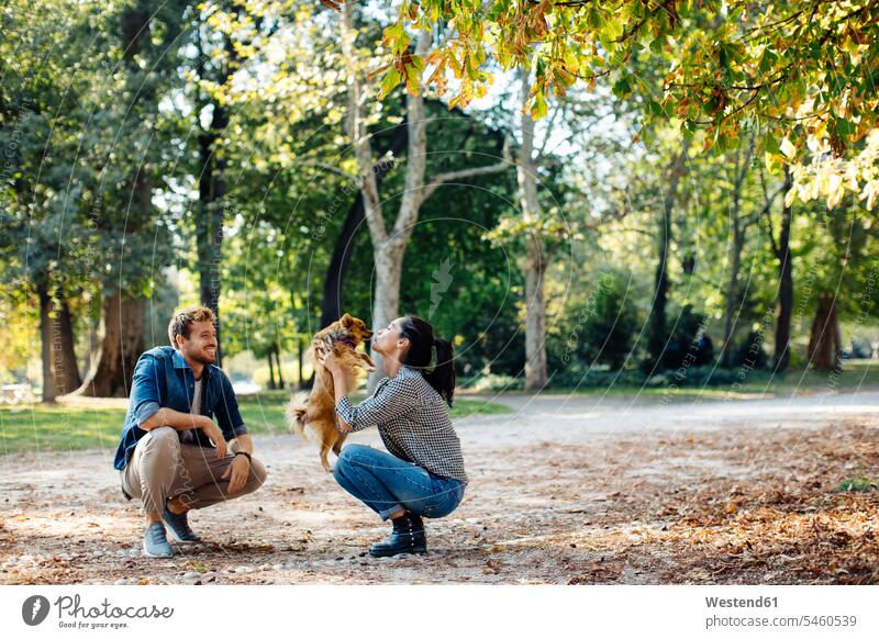 Glückliches junges Paar mit Hund in einem Park Tiere Tierwelt Haustiere Hunde entspannen relaxen Kuss Küsse freuen Frohsinn Fröhlichkeit Heiterkeit geniessen