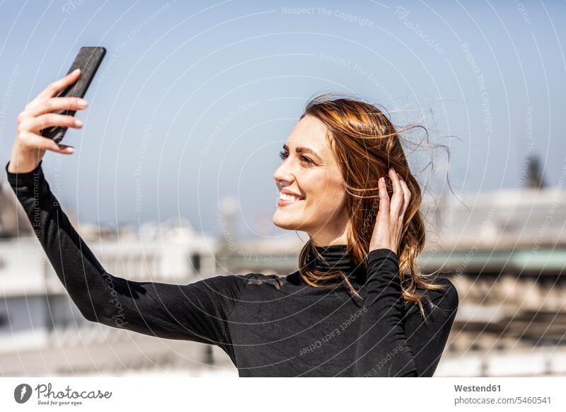 Porträt einer lächelnden Frau, die ein Selfie mit ihrem Smartphone macht weiblich Frauen Portrait Porträts Portraits Selfies iPhone Smartphones Erwachsener