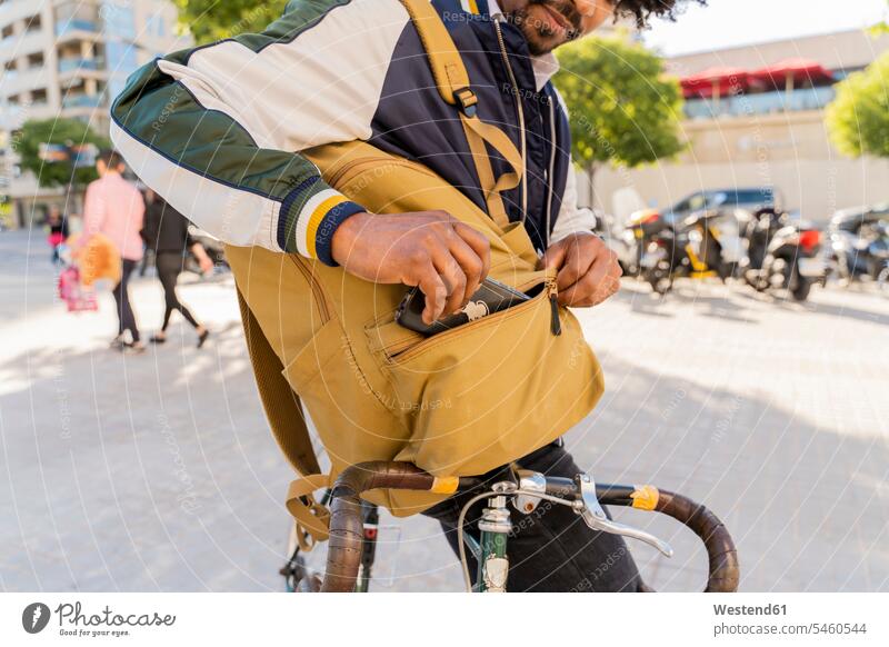 Lässiger Geschäftsmann mit Fahrrad nimmt Handy aus dem Rucksack in der Stadt, Barcelona, Spanien geschäftlich Geschäftsleben Geschäftswelt Geschäftsperson