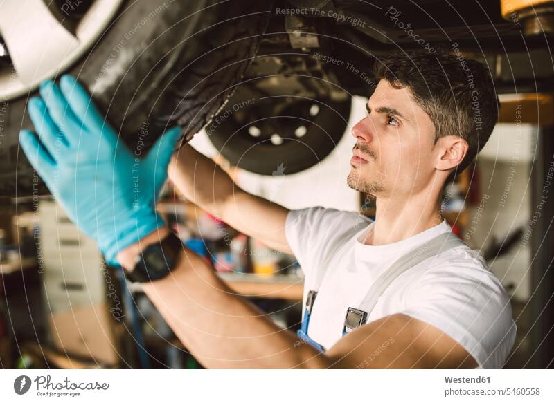 Mechaniker, der in einer Werkstatt am Unterboden eines Autos arbeitet Monteur Werkstätte Werkstaette Werkstaetten Werkstätten arbeiten Arbeit Wagen PKWs