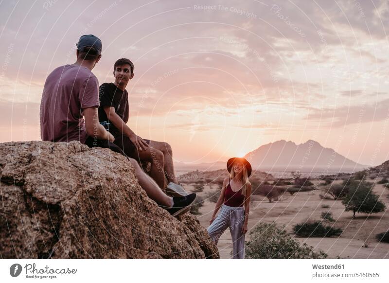 Namibia, Spitzkoppe, Freunde sitzen bei Sonnenuntergang auf einem Felsen sitzend sitzt Sonnenuntergänge Gestein Steine Freundschaft Kameradschaft Stimmung