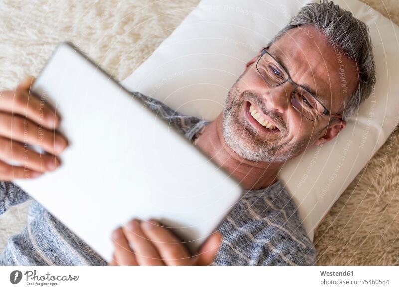 Reifer Mann, der mit einer Tablette auf einem Kissen liegt liegen liegend Männer männlich Tablet Computer Tablet-PC Tablet PC iPad Tablet-Computer Kopfkissen