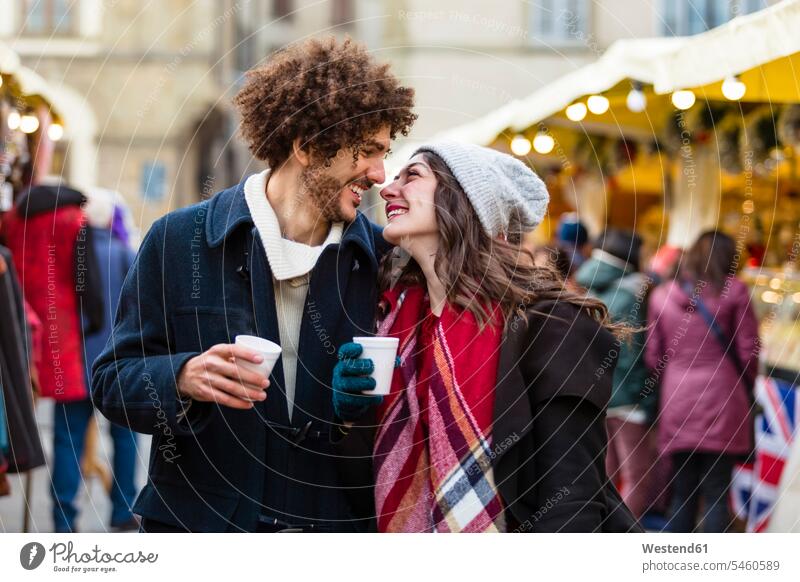 Glückliches, zärtliches junges Paar mit heißen Getränken auf dem Weihnachtsmarkt Zuneigung Heißgetränk Heissgetraenk Heissgetraenke Heißgetränke