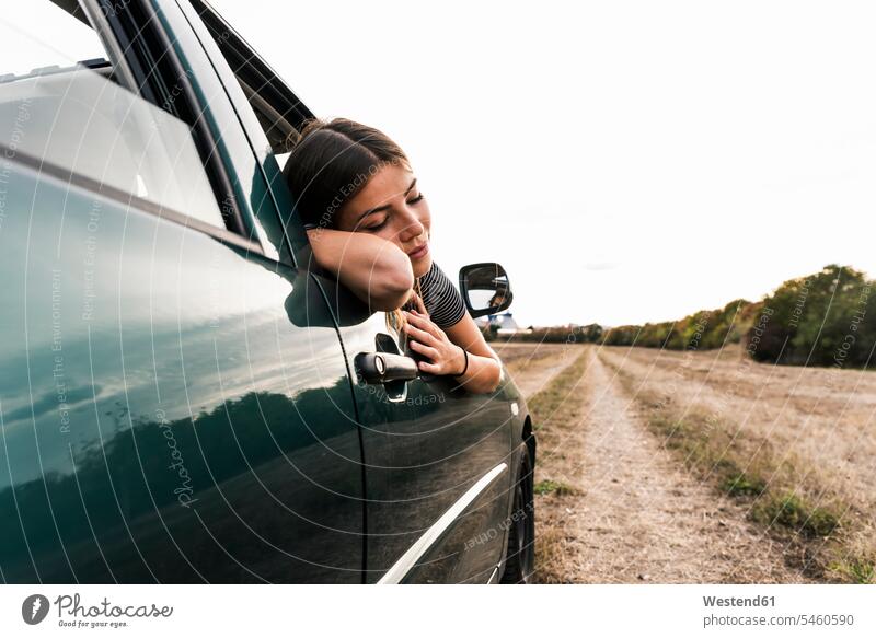 Junge Frau lehnt sich auf Feldweg aus dem Autofenster Fenster Wagen PKWs Automobil Autos Feldwege weiblich Frauen Kraftfahrzeug Verkehrsmittel KFZ Weg Wege Pfad