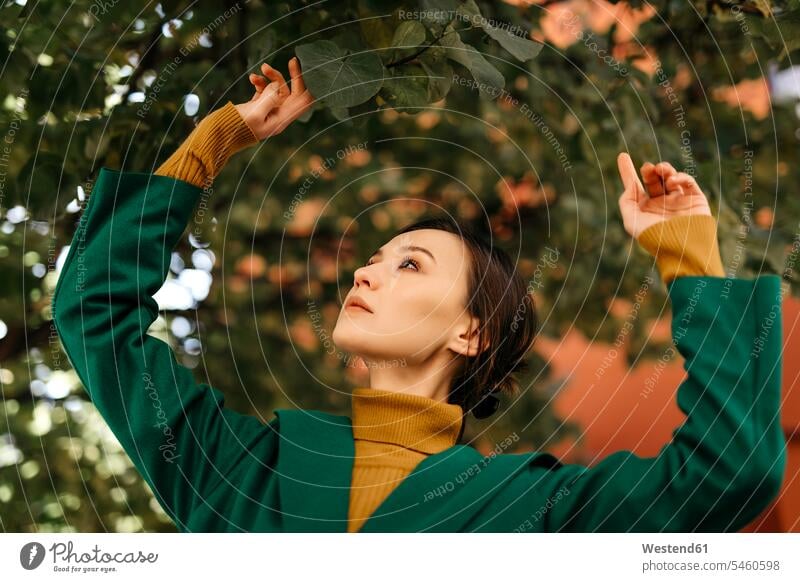 Nahaufnahme einer jungen Frau, die die Blätter eines Baumes betrachtet Farbaufnahme Farbe Farbfoto Farbphoto Spanien Freizeitkleidung Freizeitbekleidung casual