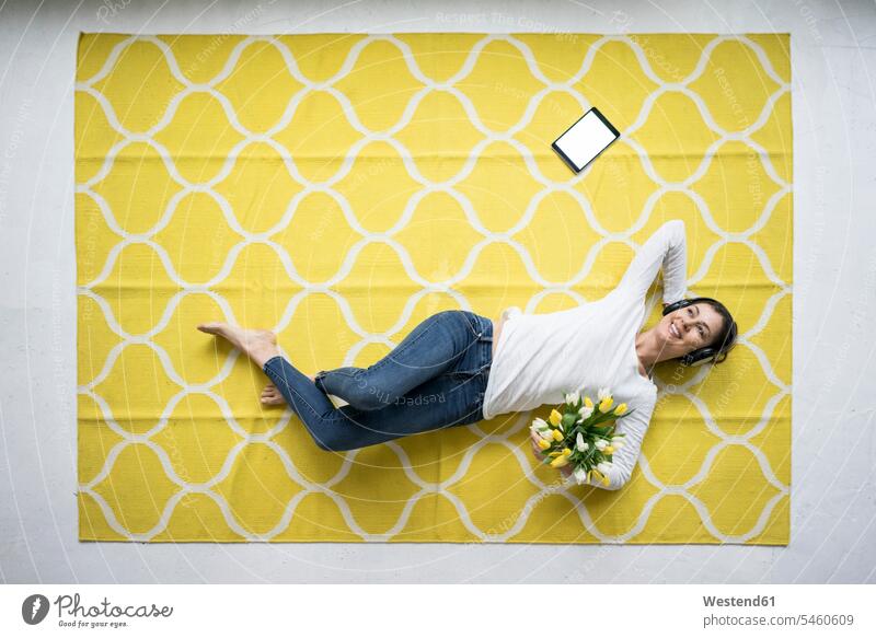 Lächelnde Frau mit Kopfhörern auf Teppich liegend mit Tulpenbüschel Blumenstrauß Bouquet Blumenstrauss Blumensträusse Blumensträuße liegt Tulipa