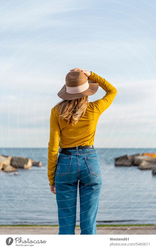 Junge Frau mit erhobenen Armen und Sonnenhut gegen das Meer Farbaufnahme Farbe Farbfoto Farbphoto Freizeitbeschäftigung Muße Zeit Zeit haben Außenaufnahme außen