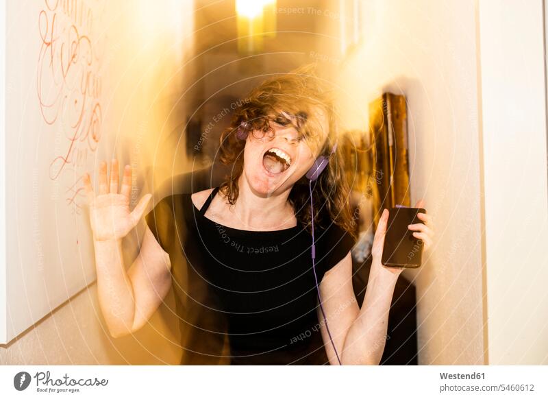 Verschwommene Bewegung einer Frau mit Kopfhörern, die zu Hause an den Wänden tanzt Farbaufnahme Farbe Farbfoto Farbphoto Deutschland Freizeitbeschäftigung Muße