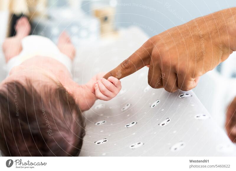 Nahaufnahme eines neugeborenen Babys, das nach dem Finger des Vaters auf dem Wickeltisch greift multikulturell Babies Säuglinge Kind Kinder greifen Griff klein
