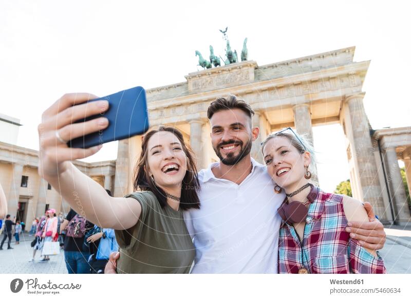 Porträt von drei glücklichen Freunden, die ein Selfie mit dem Handy vor dem Brandenburger Tor machen, Berlin, Deutschland Touristen Handies Handys Mobiltelefon