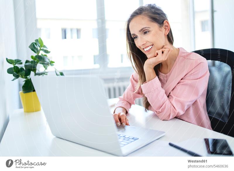 Glückliche junge Geschäftsfrau, die im Büro mit einem Laptop arbeitet Job Berufe Berufstätigkeit Beschäftigung Jobs geschäftlich Geschäftsleben Geschäftswelt