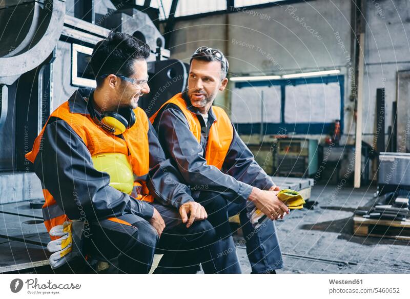 Zwei Männer in Arbeitsschutzkleidung unterhalten sich während der Pause in der Fabrik sprechen reden Mann männlich Schutzkleidung Fabrikgebäude Fabrikgebaeude