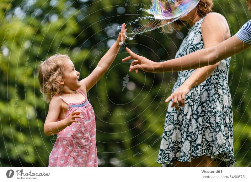 Mädchen explodiert Blase beim Spielen mit der Familie im Park Farbaufnahme Farbe Farbfoto Farbphoto Außenaufnahme außen draußen im Freien Tag Tageslichtaufnahme