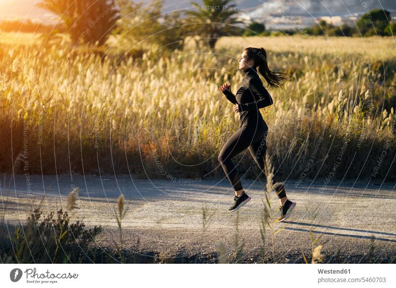 Junge Frau läuft auf Fußweg gegen grüne Landschaft bei Sonnenuntergang Farbaufnahme Farbe Farbfoto Farbphoto Spanien Sportkleidung Sportbekleidung Sportdress