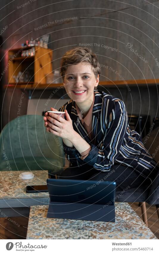 Porträt eines lächelnden Freiberuflers, der mit digitalem Tablet und Smartphone in einem Café sitzt geschäftlich Geschäftsleben Geschäftswelt Geschäftsperson