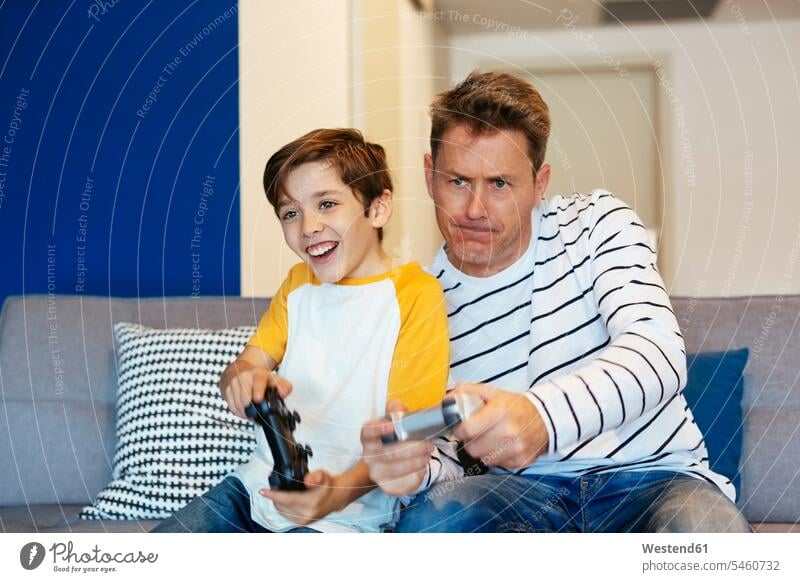 Vater und Sohn spielen zu Hause auf der Couch Videospiele Söhne Sofa Couches Liege Sofas Zuhause daheim Papas Väter Vati Vatis Papis Kind Kinder Familie