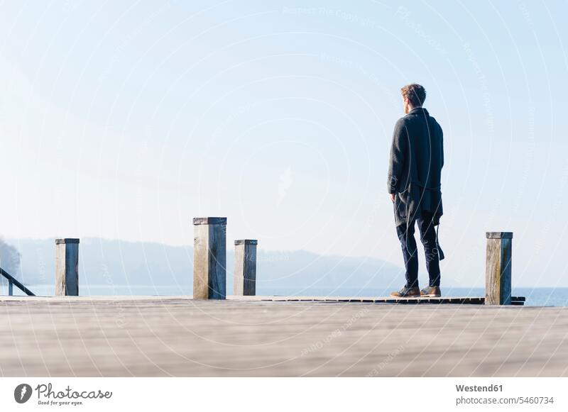 Mann schaut bei klarem Himmel auf den See, während er an einem sonnigen Tag auf dem Pier steht Farbaufnahme Farbe Farbfoto Farbphoto Deutschland Außenaufnahme