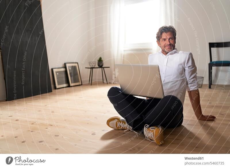 Porträt eines lächelnden reifen Mannes mit Laptop, der zu Hause auf dem Boden sitzt Rahmen Technik Technologien E Mail E Mails E-Mails electronic mail