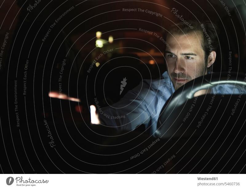 Junger Mann im Auto bei Nacht Hemd Hemden Navigationssystem Fahrzeuginnenraum dunkel mobiles Arbeiten mobile working schauen sehend Erreichbarkeit verfügbar