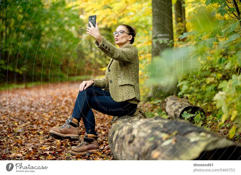 Reife Frau nimmt ein Selfie in einem Herbstwald Jacken Telekommunikation telefonieren Handies Handys Mobiltelefon Mobiltelefone Brillen entspannen relaxen