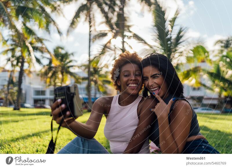 Zwei glückliche Freundinnen machen ein Sofortfoto in einem Park Glück glücklich sein glücklichsein Parkanlagen Parks entspannt entspanntheit relaxt Sofortbild