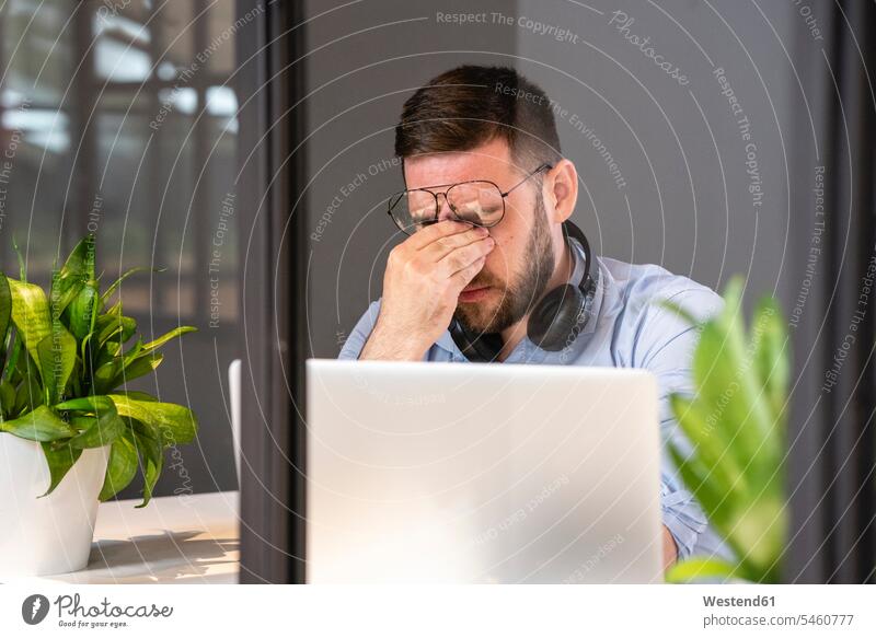 Müde, gut aussehender männlicher Profi mit Laptop durch Glaswand im Büro für kreative Zusammenarbeit gesehen Farbaufnahme Farbe Farbfoto Farbphoto Geschäftsmann