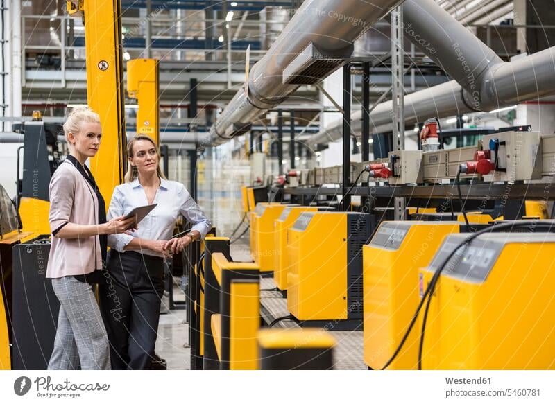 Zwei Frauen mit Tablette Blick auf Maschine in der Fabrik Shop Floor Fabriken weiblich Maschinen ansehen Fabrikhalle Industriehallen Fabrikhallen