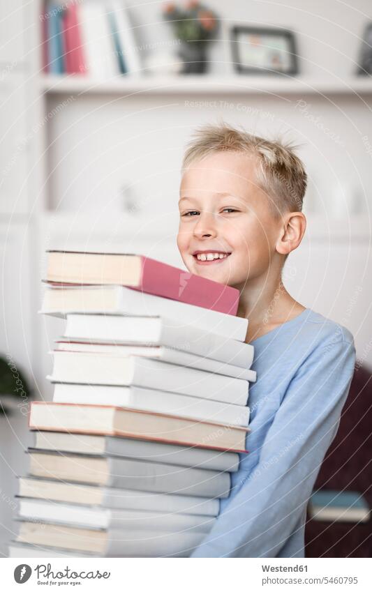 Porträt eines lächelnden blonden Jungen, der einen Stapel Bücher trägt Lektüre freuen Glück glücklich sein glücklichsein zufrieden daheim zu Hause Muße