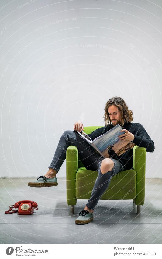 Junger Mann liest Buch, während er zu Hause auf einem Sessel an der Wand sitzt Farbaufnahme Farbe Farbfoto Farbphoto Spanien Freizeitbeschäftigung Muße Zeit