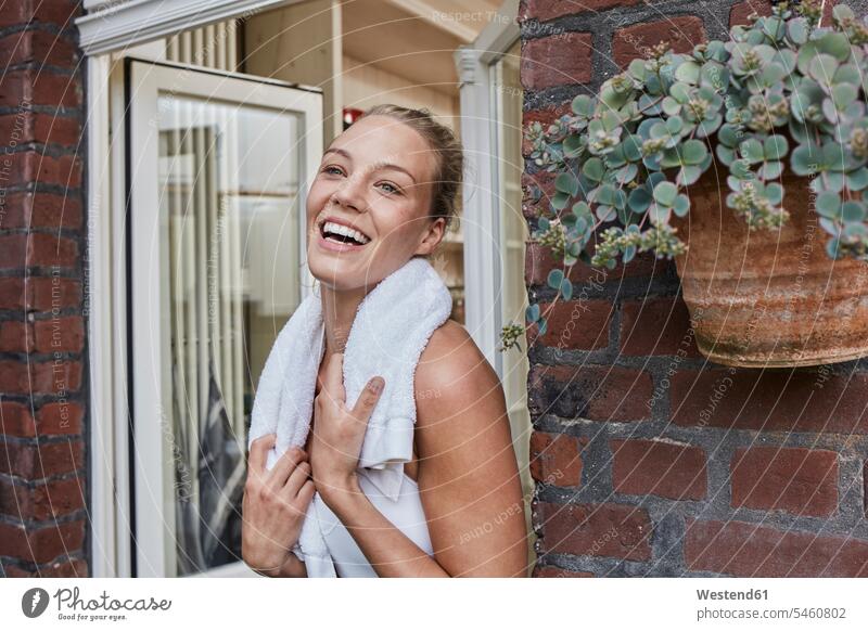 Glückliche sportliche junge Frau mit Handtuch um den Hals am Hauseingang Handtuecher Handtücher glücklich glücklich sein glücklichsein weiblich Frauen Sport