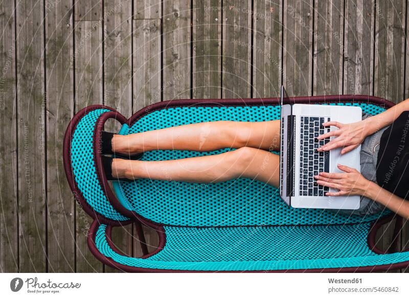 Junge Frau sitzt auf türkisfarbener Couch auf der Terrasse und benutzt einen Laptop, Ansicht von oben Sofa Couches Liege Sofas Terrassen weiblich Frauen sitzen