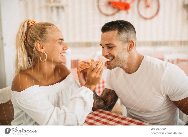 Fröhliche junge Frau füttert ihren Freund mit Pizza, während sie im Restaurant sitzt Farbaufnahme Farbe Farbfoto Farbphoto Spanien Freizeitbeschäftigung Muße
