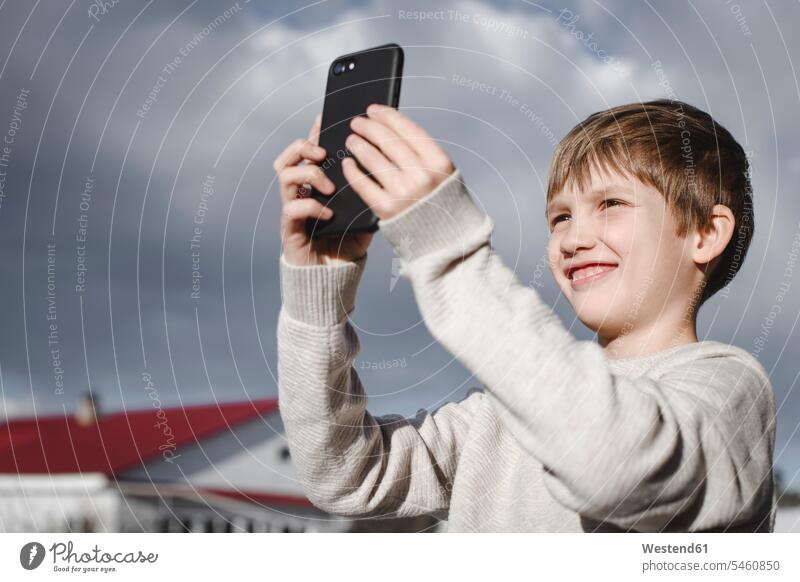 Porträt eines glücklichen Jungen, der ein Selfie mit seinem Smartphone macht iPhone Smartphones Buben Knabe Knaben männlich Glück glücklich sein glücklichsein