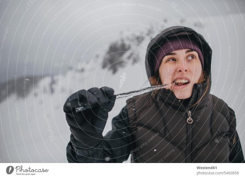 Österreich, Kitzbühel, Porträt einer jungen Frau, die auf einen Eiszapfen beißt weiblich Frauen abbeißen abbeissen Portrait Porträts Portraits Erwachsener