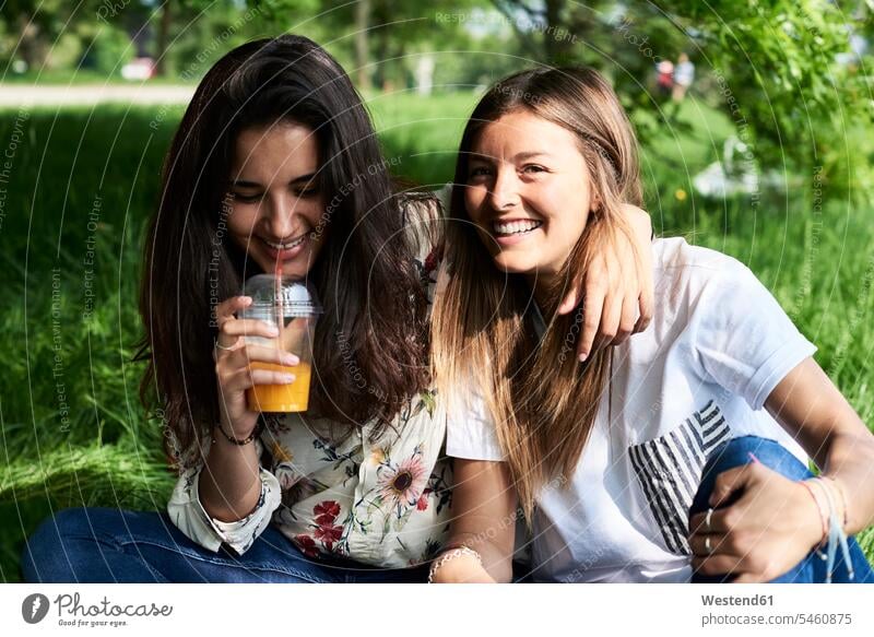 Porträt von zwei glücklichen jungen Frauen trinken Saft bei einem Picknick im Park Glück glücklich sein glücklichsein Parkanlagen Parks weiblich Portrait