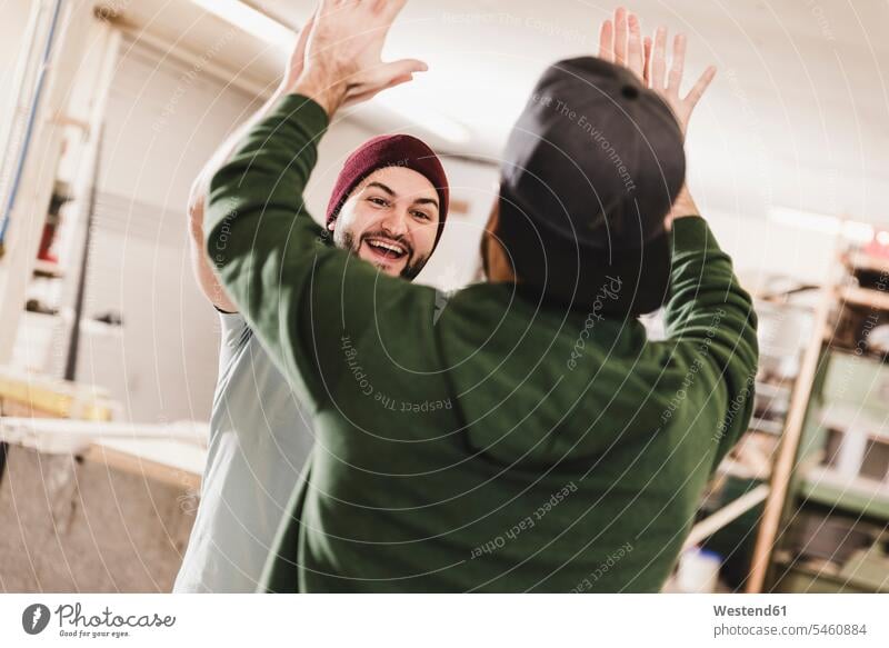 Zwei glückliche junge Männer geben sich in einem Workshop die Klinke in die Hand Kollegen Arbeitskollegen Werkstatt Werkstätte Werkstaette Werkstaetten