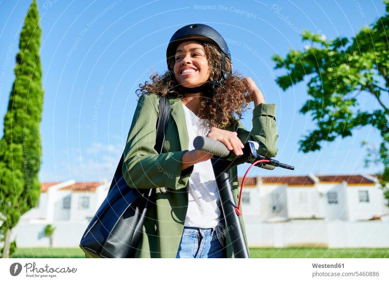 Glückliche Frau, die an einem sonnigen Tag mit einem elektrischen Roller steht Farbaufnahme Farbe Farbfoto Farbphoto Außenaufnahme außen draußen im Freien