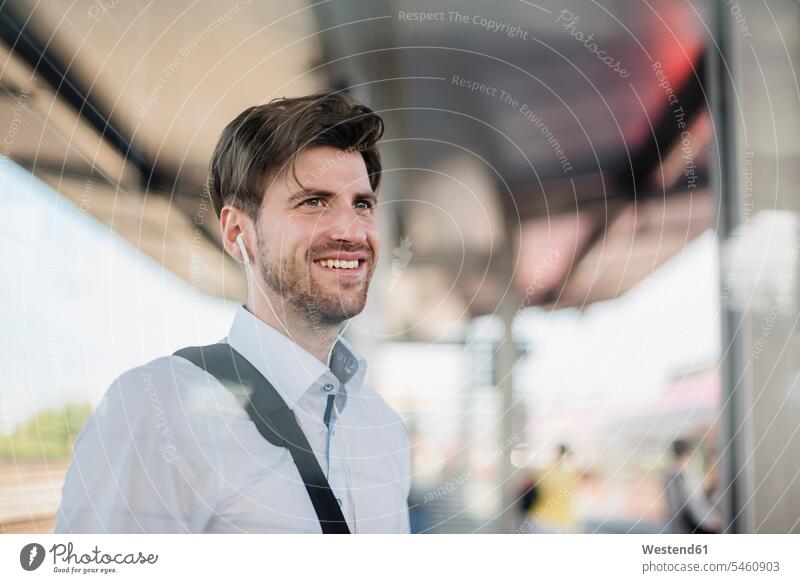 Porträt eines lächelnden Geschäftsmannes auf einem Bahnsteig mit Kopfhörern Businessmann Businessmänner Geschäftsmänner Portrait Porträts Portraits Zugbahnsteig