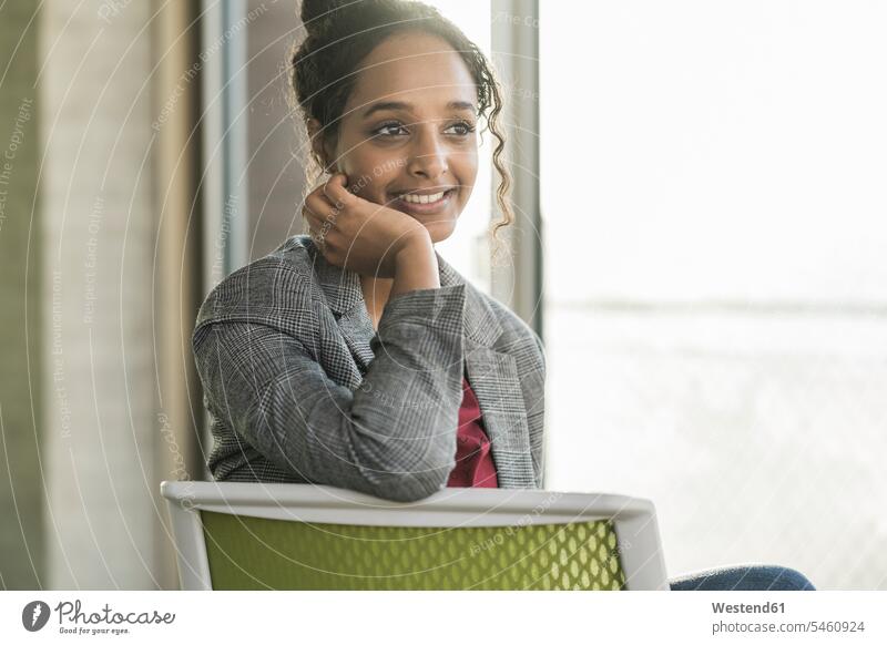 Lächelnde junge Geschäftsfrau sitzt im Büro auf einem Stuhl Job Berufe Berufstätigkeit Beschäftigung Jobs Leute Menschen People Person Personen gelockt