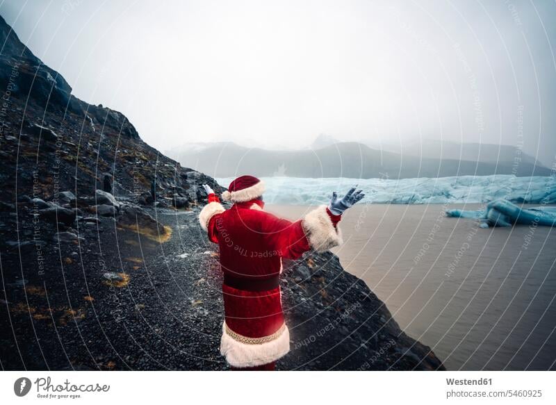 Island, Rückansicht des Weihnachtsmanns vor Gletscher stehend Weihnachtsmänner Weihnachtsmaenner Santa Claus Nikolaus steht Eis Ice Weihnachten Christmas X-Mas