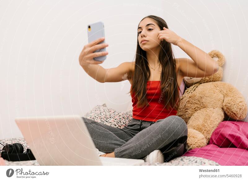 Teenager-Mädchen sitzt mit der Hand in den Haaren, während sie zu Hause ein Mobiltelefon benutzt Farbaufnahme Farbe Farbfoto Farbphoto Innenaufnahme