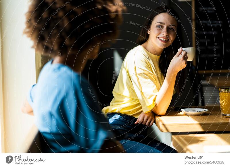 Glückliche Frau hält Kaffeetasse in der Hand, während sie einen Freund im Café besucht Farbaufnahme Farbe Farbfoto Farbphoto Innenaufnahme Innenaufnahmen innen