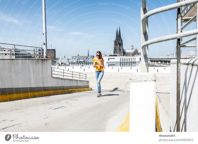 Deutschland, Köln, Frau, die mit dem Handy auf einer Rampe auf Höhe des Parkplatzes läuft benutzen Parkdeck Parkdecks weiblich Frauen Smartphone iPhone