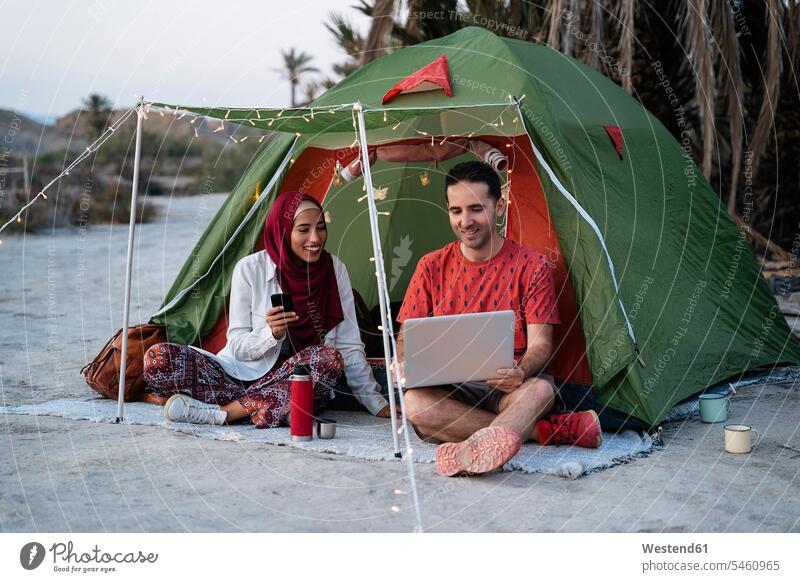 Junge Frau mit Hijab und Mann mit Laptop in einem Zelt Kopftücher Rechner Laptops Notebook Notebooks Telekommunikation telefonieren Handies Handys Mobiltelefon