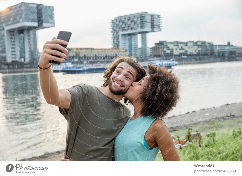 Deutschland, Köln, glückliches Paar bei einem Selfie am Flussufer Glück glücklich sein glücklichsein Portrait Porträts Portraits entspannt entspanntheit relaxt