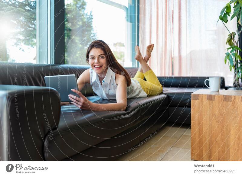 Porträt einer glücklichen Frau, die zu Hause auf einer Couch liegt und ein Tablett benutzt liegen liegend Portrait Porträts Portraits Tablet Computer Tablet-PC