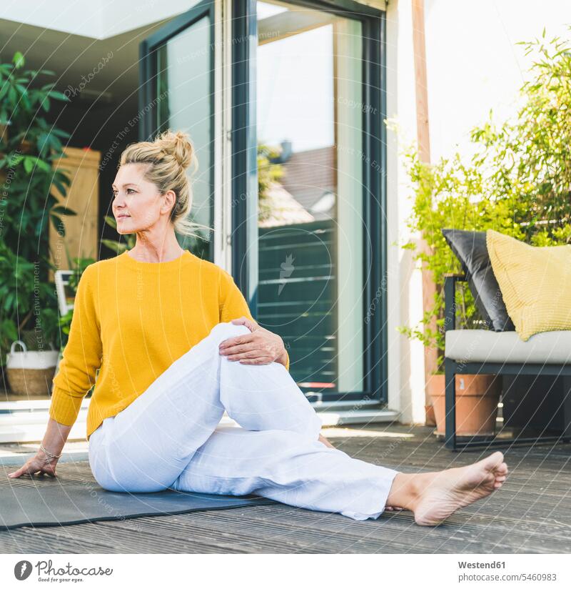 Reife Frau macht Yoga-Übungen auf der Terrasse entspannen relaxen sitzend sitzt Farben Farbtoene Farbton Farbtöne gelbe gelber gelbes daheim zu Hause Muße