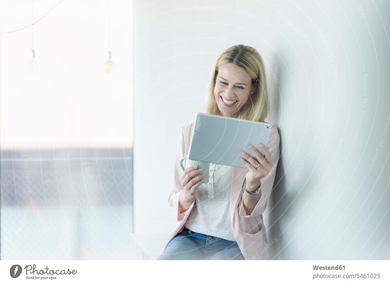 Glückliche Geschäftsfrau lehnt gegen eine Wand mit Tablette Deutschland offenes Lächeln lachen offenes Laecheln Drahtlose Technologie drahtlose Verbindung