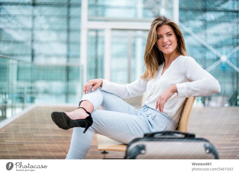 Lächelnde junge Geschäftsfrau sitzt im Freien mit Koffer und schaut sich um sitzen sitzend Geschäftsfrauen Businesswomen Businessfrauen Businesswoman lächeln