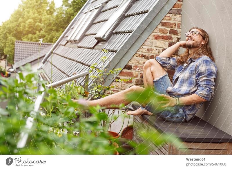 Glücklicher junger Mann sitzt auf seinem Balkon und entspannt sich Pflanze Pflanzenwelt Flora junge Männer glücklich glücklich sein glücklichsein sitzen sitzend